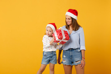 Woman child baby girl in Christmas Santa hat hold gift box. Mommy little kid daughter isolated on yellow background studio portrait. Happy New Year 2020 celebration holiday concept. Mock up copy space