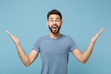 Young surprised attractive man in casual clothes posing isolated on blue background studio portrait. People sincere emotions lifestyle concept. Mock up copy space. Keeping mouth open, spreading hands.