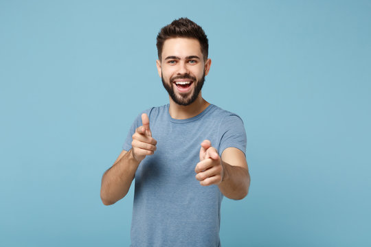 Young cheerful handsome man in casual clothes posing isolated on blue wall background, studio portrait. People sincere emotions lifestyle concept. Mock up copy space. Pointing index fingers on camera.