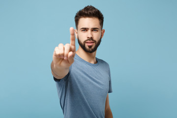 Young man in casual clothes posing isolated on blue background in studio. People lifestyle concept. Mock up copy space. Touch something like push click on button, pointing at floating virtual screen.