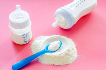 Baby food. Powder in spoon near baby bottle on pink background