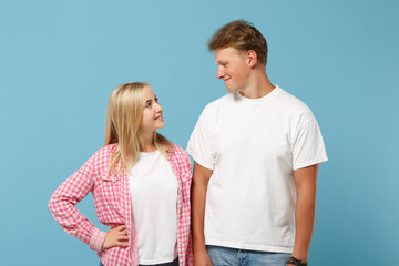 Young couple two friends guy girl in white pink empty blank design t-shirts posing isolated on pastel blue background studio portrait. People lifestyle concept. Mock up copy space. Looking each other.