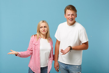 Young fun couple two friends guy girl in white pink empty blank design t-shirts posing isolated on pastel blue background studio portrait. People lifestyle concept. Mock up copy space. Looking upset.