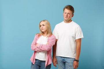Young fun couple two friends guy girl in white pink empty blank design t-shirts posing isolated on pastel blue background studio portrait. People lifestyle concept. Mock up copy space. Looking upset.