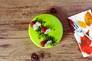 chic pistachio cake decorated with raspberry, white chocolate flower and chopped pistachio, elegant cake on a wooden table