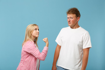 Young couple two friends guy girl in white pink empty blank design t-shirts posing isolated on pastel blue background in studio. People lifestyle concept. Mock up copy space. Swearing, clenching fist.