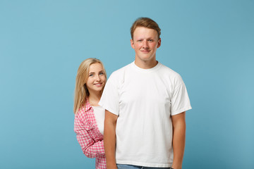 Fototapeta premium Young smiling beautiful couple two friends guy girl in white pink empty blank design t-shirts posing isolated on pastel blue background, studio portrait. People lifestyle concept. Mock up copy space.