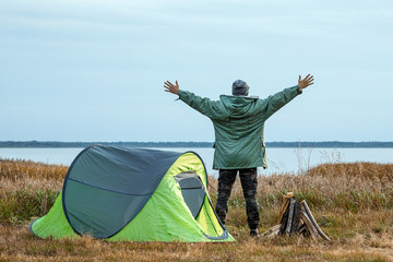 A bearded man near a camping tent in green on the background of nature and the lake. The concept of travel, tourism, camping.