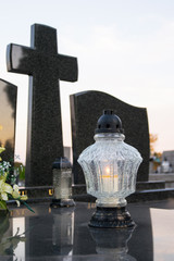 Granitowy pomnik z krzyżem. Zapalony znicz na cmentarzu katolickim.