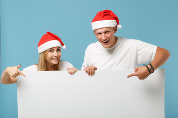 Smiling young Santa couple friends guy girl in Christmas hat isolated on blue background. Happy New Year 2020 celebration holiday concept. Mock up copy space. Holding big white empty blank billboard.
