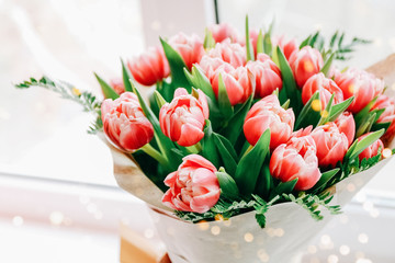 Beautiful bouquet of pink tulips wrapped in paper on windowsill background
