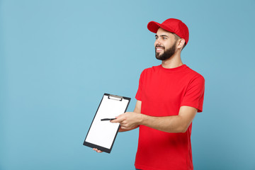 Delivery man in red uniform isolated on blue background, studio portrait. Professional male employee in cap t-shirt print working as courier dealer hold clipboard. Service concept. Mock up copy space.