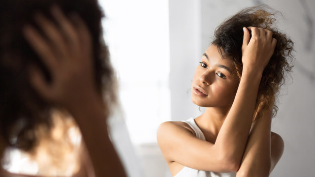 Afro Woman Touching Hair Looking In Mirror In Bathroom, Panorama