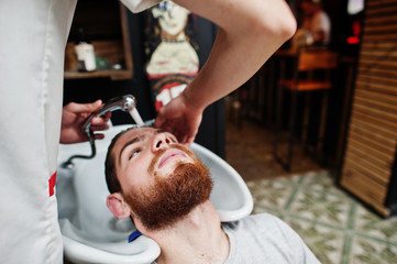 Obraz na płótnie Canvas Young bearded man washing head by hairdresser while sitting in chair at barbershop. Barber soul.