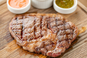 Sliced medium rare grilled Steak Ribeye with Pickled cabbage and two sauces. Serving on a wooden Board. Barbecue restaurant menu, a series of photos of different meats.