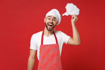 Excited young bearded male chef cook or baker man in striped apron toque chefs hat isolated on red background in studio. Cooking food concept. Mock up copy space. Holding say cloud with lightbulb.