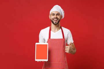 Cheerful chef cook or baker man in striped apron toque chefs hat isolated on red background. Cooking food concept. Mock up copy space. Hold tablet pc computer with blank empty screen showing thumb up.