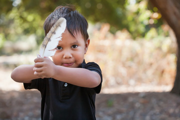 A litte boy holding a birds feather like a sword in a crown guard position.