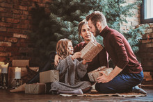 Cute happy girl is giving present for her parents while sitting all together under christmas tree.