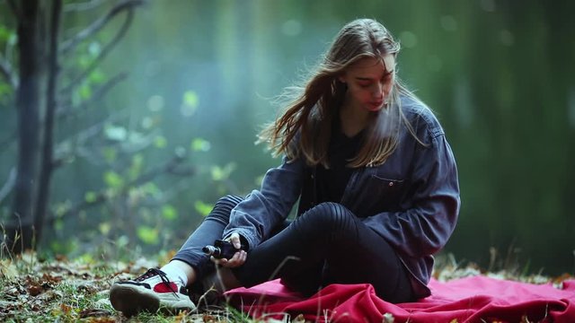 Vape teenager. Young beautiful white teenage girl in casual clothes vaping electronic cigarette near the river on the street in the park in the autumn evening. Bad habit. Vaping activity.