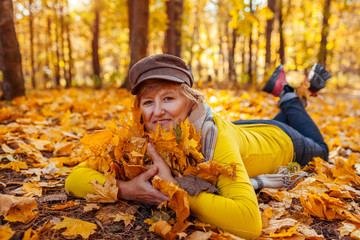 Fall activities. Woman lying on heap of leaves in autumn park. Senior woman having fun outdoors