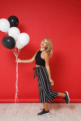 Beautiful young woman girl in black clothes posing isolated on red background studio portrait. St. Valentine's Day birthday holiday party concept. Mock up copy space. Celebrating holding air balloons.