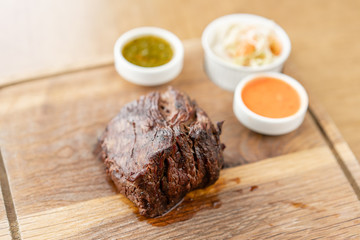 Fried dry aged beef fillet chateaubriand medallion steak natural with Pickled cabbage and two sauces. Serving on a wooden Board. Barbecue restaurant menu.