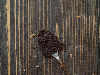 teaspoon full of tea leaf on a wooden table. black tea in a spoon