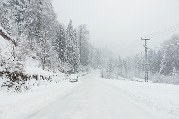 Fototapeta na wymiar Snowy road in winter with an SUV parked.