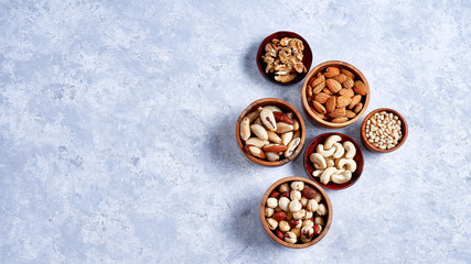 pecans, hazelnuts, almonds, pine nuts, Brazil nut, cashews in wooden bowls on blue background, top...