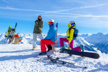 Four happy friends snowboarders and skiers are having fun on ski slope with ski and snowboards in...