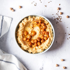 Hummus with olive oil and chickpeas in a ceramic bowl on a light grey background