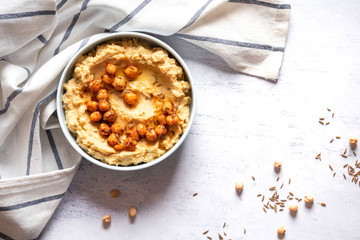 Hummus with olive oil and chickpeas in a ceramic bowl on a light grey background