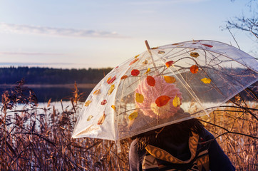 A woman in a pink knitted hat under transparent umbrella in autumn