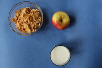 milk and corn flakes and an Apple on a blue background