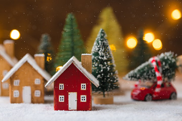 Miniature wooden houses and small red car with fir tree on the snow over blurred Christmas decoration background, toned
