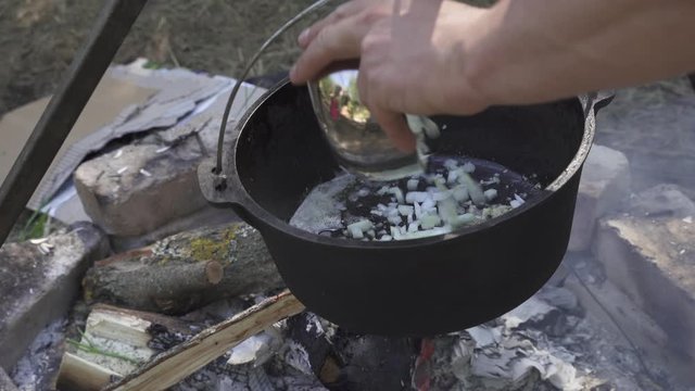 Frying onion for girolle (Cantharellus cibarius), Porcini (Boletus) mushroom and chicken risotto in cast iron pot on an open campfire