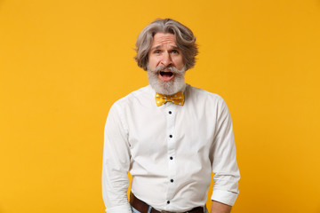 Shocked nervous elderly gray-haired mustache bearded man in white shirt, bow tie posing isolated on yellow background studio portrait. People lifestyle concept. Mock up copy space. Keeping mouth open.