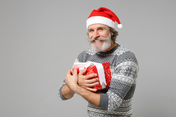 Smiling elderly gray-haired mustache bearded Santa man in sweater Christmas hat isolated on grey background. New Year 2020 celebration holiday concept. Mock up copy space. Hold present box with gift.