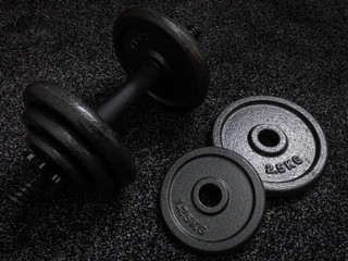 Obraz na płótnie Canvas 1.25 kg and 2.5 kg weight plates with dumbbell beside on dark background.