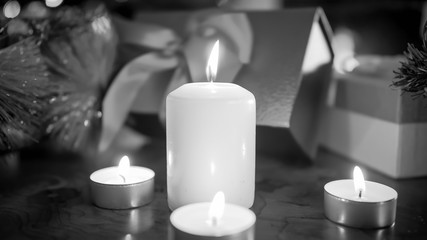 Closeup black and white image of burning candles aginst Christmas gifts and presents
