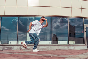 dancer dancing break dance, hip hop. In summer city, background glass windows. Active youth lifestyle, young male dancer, fitness workout breakdancer jeans sneakers, sunglasses. Free space for text.