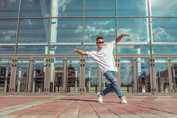 Fototapeta na wymiar Dancer in motion dancing break dance, hip hop. In summer city, background glass windows clouds. Active youth lifestyle, young male, fitness movement workout breakdancer. Free space for text.