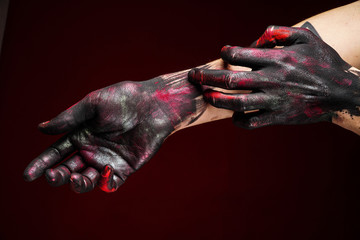 Men's hand in black, pink and red paint scratching another arm on a dark background. Close-up