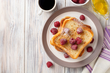 French toasts with powdered sugar and fresh raspberries on wooden table. Top view. Copy space.