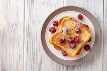 French toasts with powdered sugar and fresh raspberries on wooden table. Top view. Copy space.