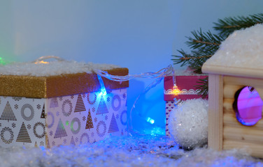 a small wooden house and a gift box on the grass near the Christmas tree in the snow. Christmas decorations. Christmas theme