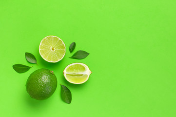 Fresh juicy lime and green leaves on bright green background. Top view flat lay copy space. Creative food background, tropical fruit, vitamin C, citrus. Composition with whole and slices of lime