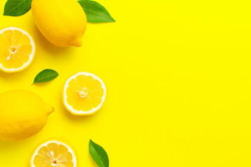 Creative background with fresh lemons and green leaves on bright yellow background. Top view flat...