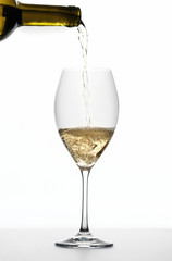 Glass of white wine pouring from a bottle.